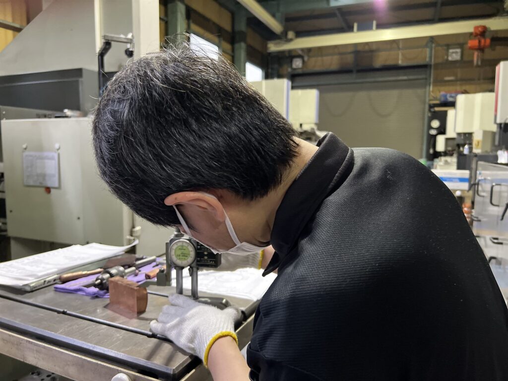 ダイヤルゲージで銅電極の寸法を実測検査している様子